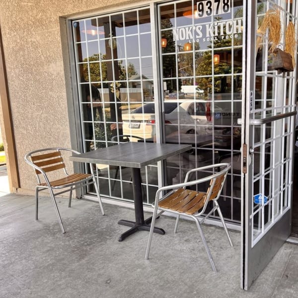 Outdoor seating area with a small table and two chairs in front of Nok's Kitchen.