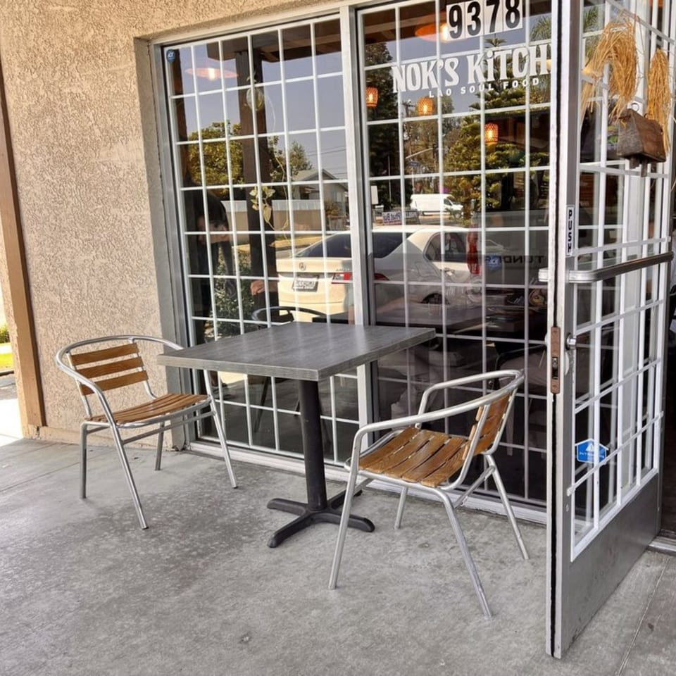 Outdoor seating area with a small table and two chairs in front of Nok's Kitchen.