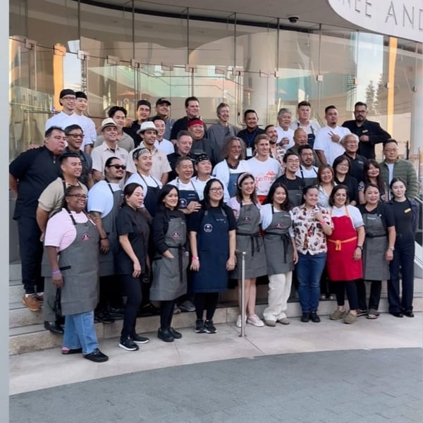 A large group of diverse chefs and staff from Nok's Kitchen posing on steps outside a building.