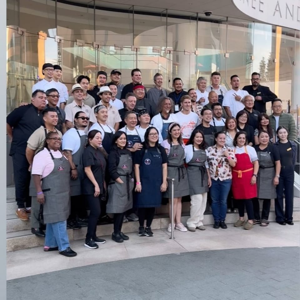 A large group of diverse chefs and staff from Nok's Kitchen posing on steps outside a building.