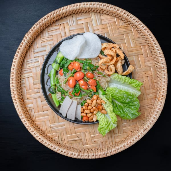 Nok's Kitchen's Lao dish with noodles, vegetables, peanuts, pork rinds, and shrimp crackers on a woven tray.