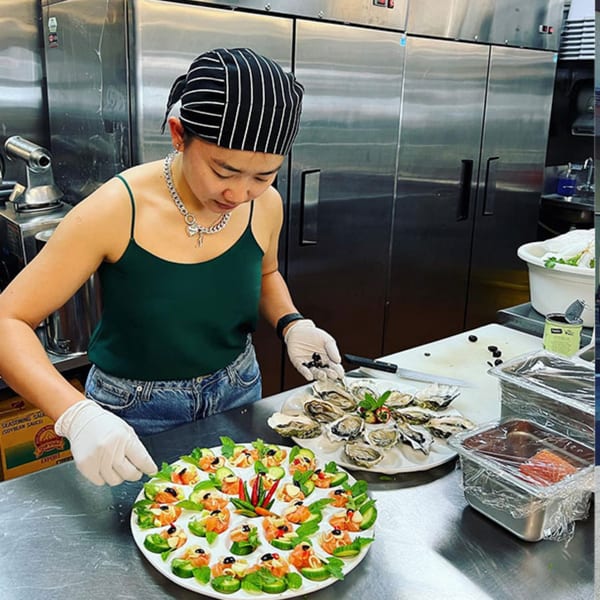 Chef in a commercial kitchen preparing plates of fresh oysters and salmon appetizers.